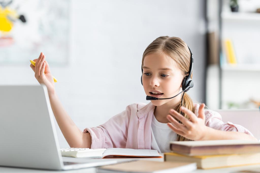 Selective focus of child in headset talking during webinar near books at home  - Photo, Image