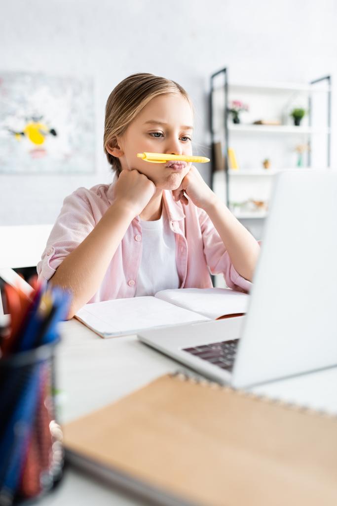自宅で電子学習中に唇の近くにペンを保持している子供の選択的な焦点  - 写真・画像