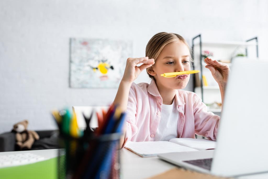 Вибірковий фокус дитини тримає ручку біля рота під час вебінару на ноутбуці вдома
  - Фото, зображення