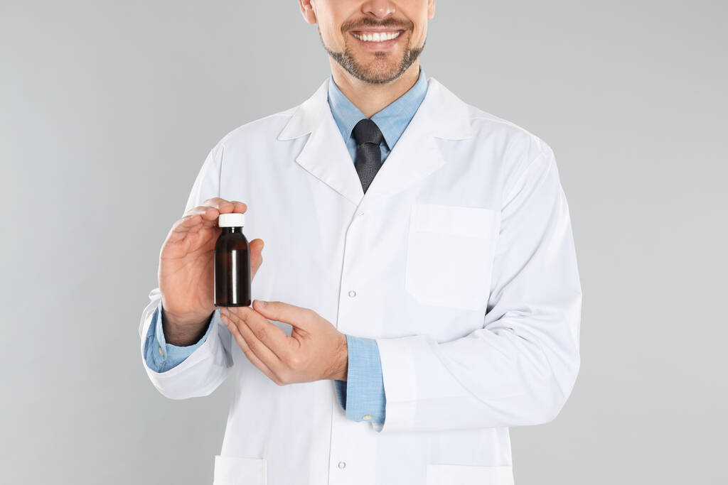 Professional pharmacist with syrup on light grey background, closeup - Photo, Image