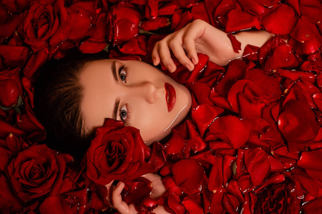 美しさの肖像画、赤いバラの花びらを持つバスルームで若い女性、トップビュー、きれいな肌を持つモデルは、レタッチ。スキンケアコンセプト. - 写真・画像