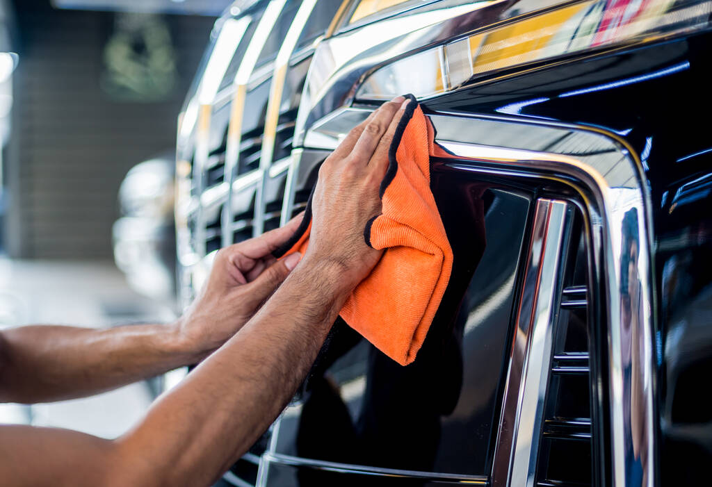 Serwis samochodowy pracownik polerowanie samochodu z mikrofibry tkaniny. - Zdjęcie, obraz