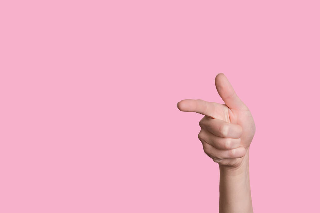 Die Hand zeigt die Geste einer Waffe oder nach links. Vereinzelter rosa Hintergrund. - Foto, Bild