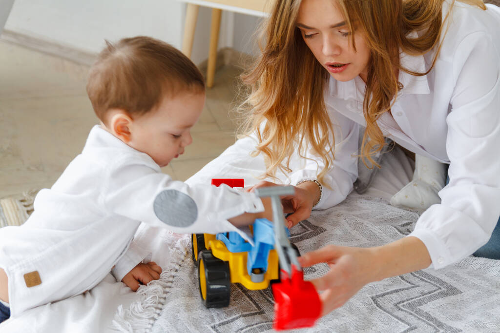 Giovane madre e figlio carino giocare insieme con un trattore giocattolo seduto sul letto - Foto, immagini
