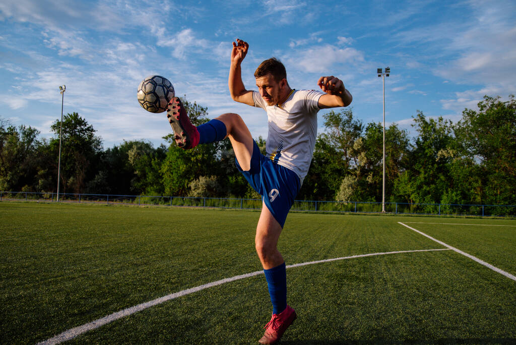 Fiatal férfi focista zsonglőrködik egy labdát a focipályán.Athlete zsonglőrködik a labdarúgás a lábát a stadionban.Football sport koncepció - Fotó, kép