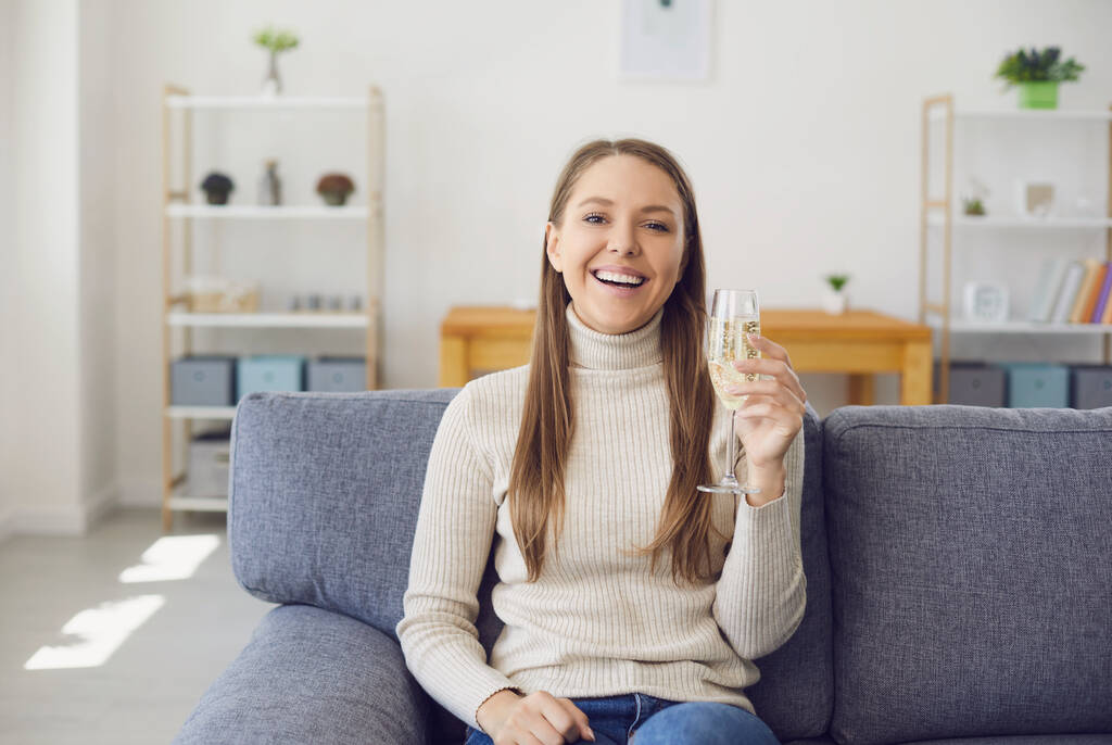 Девушка с бокалом вина смотрит в камеру, улыбаясь дома.
. - Фото, изображение