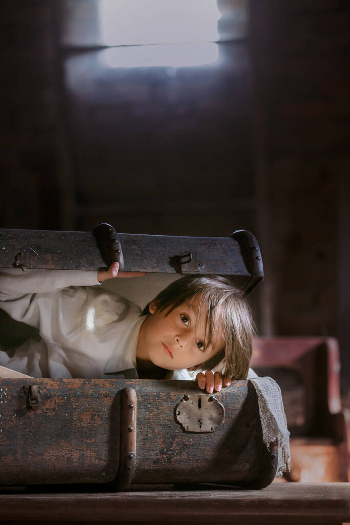 Μικρό παιδί, αγόρι, κρύβεται σε παλιά παλιά βαλίτσα στη σοφίτα, φοβάται να μην βρεθεί - Φωτογραφία, εικόνα