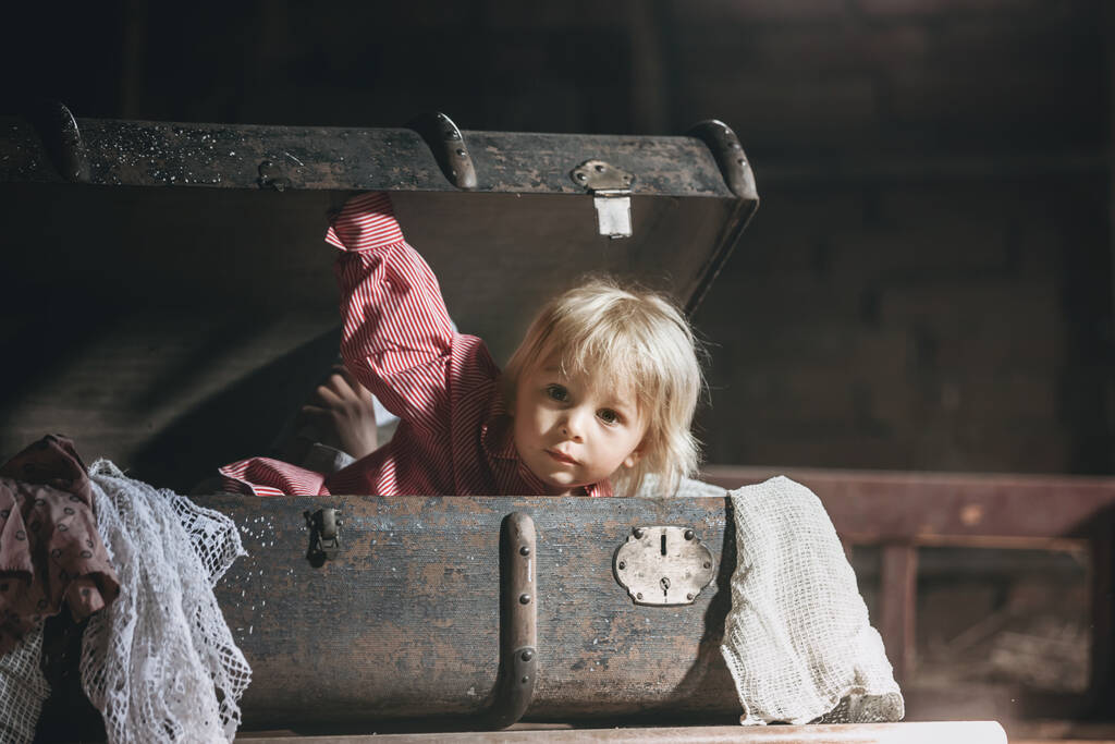 Μικρό παιδί, αγόρι, κρύβεται σε παλιά παλιά βαλίτσα στη σοφίτα, φοβάται να μην βρεθεί - Φωτογραφία, εικόνα