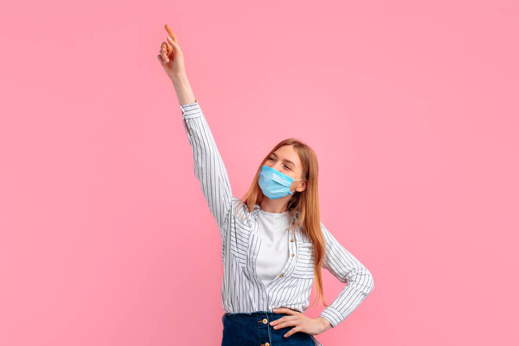 woman in a medical protective mask on her face, rejoicing and celebrating the victory, on a pink background - Photo, Image