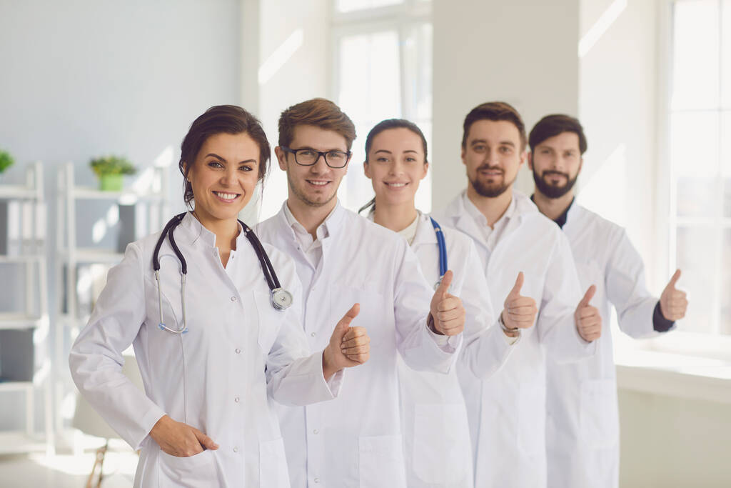 Joven equipo de médicos sonrientes retrato con pulgares hacia arriba gesto en la oficina del hospital clínico moderno
. - Foto, imagen