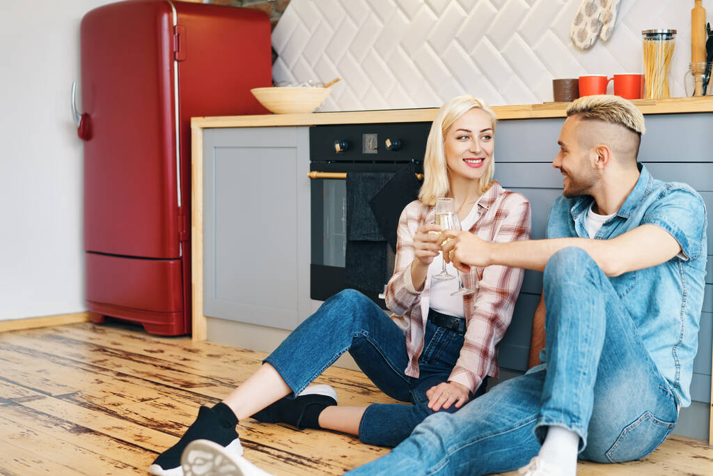 ロマンチックな幸せなカップルはキッチンで床に座って、シャンパングラスを乾杯 - 写真・画像