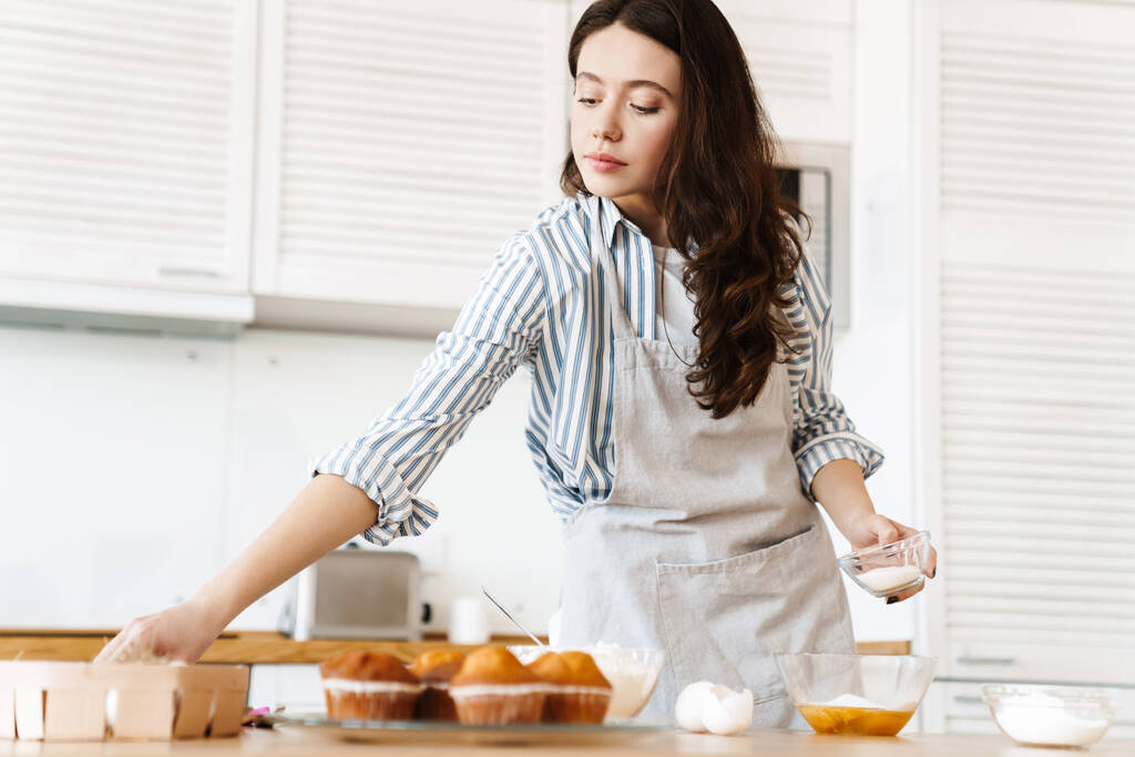 Image of focused young woman wearing apron preparing dough while cooking pie in modern kitchen - Photo, Image
