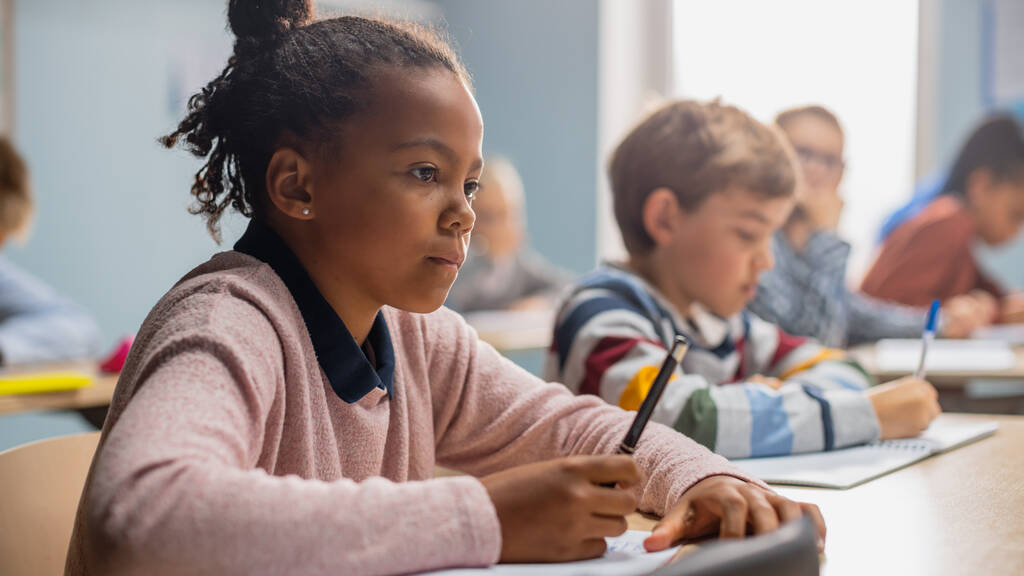 小学校の教室では、鮮やかな黒の女の子は、演習ノートに書き込みテストと筆記試験を取る。多様な子どもたちが勤勉に働き、新しいことを学ぶジュニアクラス - 写真・画像