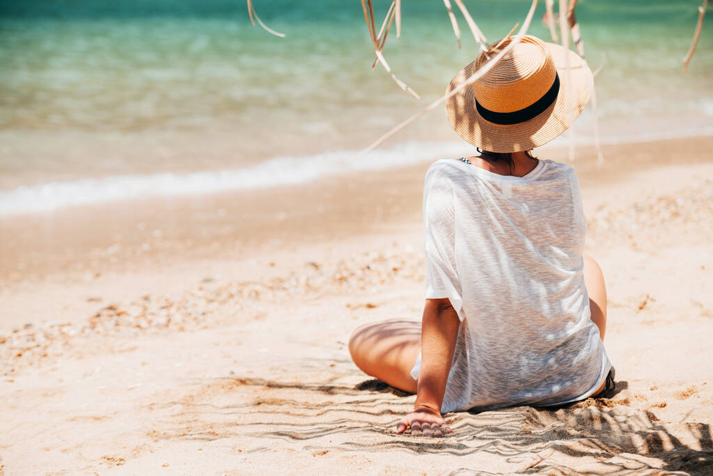 Женщина, сидящая на морском пляже в тени пальмы. Концепция безопасного загара
 - Фото, изображение