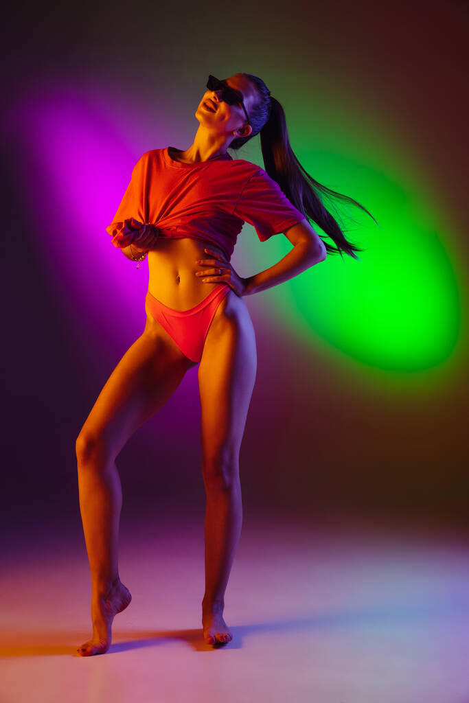 Beautiful seductive girl in fashionable swimsuit on disco bicolored neon studio background in neon light. Summer, resort, fashion and weekend concept - Photo, Image
