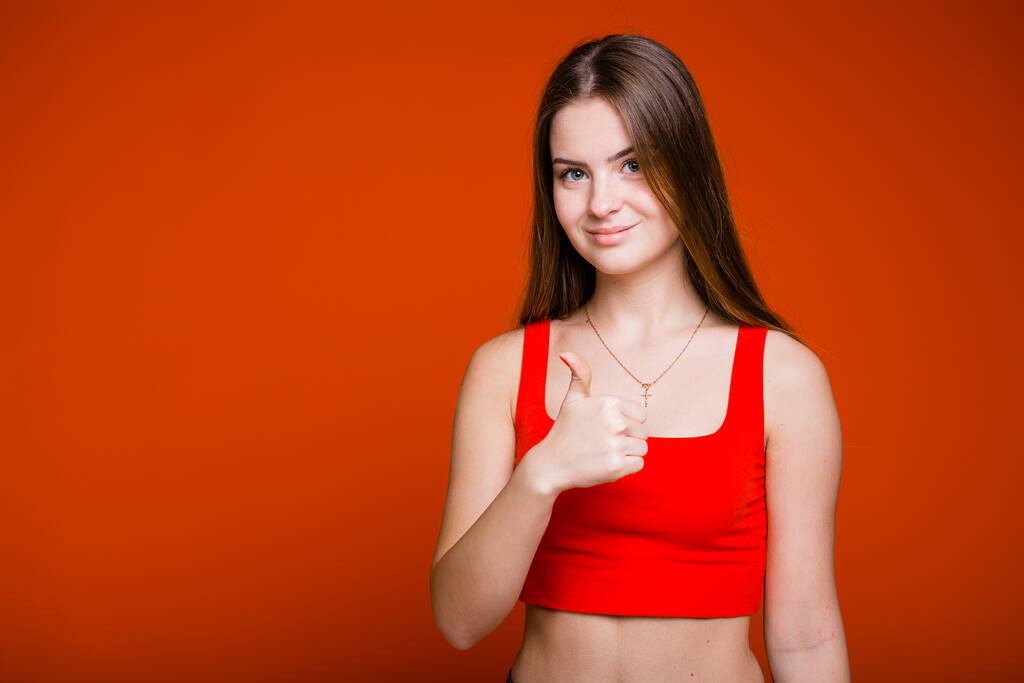Naismuotokuva tytöstä punaisessa t-paidassa, joka katsoo kameraan ja näyttää kuin käsi oranssilla pohjalla. - Valokuva, kuva