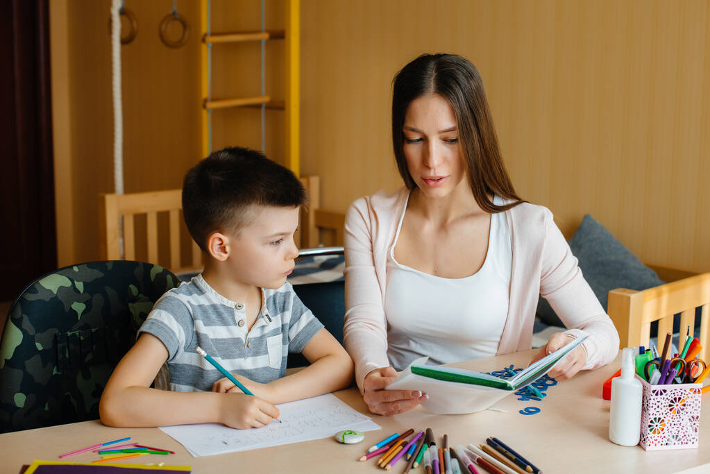 Een jonge moeder doet huiswerk met haar zoon thuis. Ouders en opleiding - Foto, afbeelding