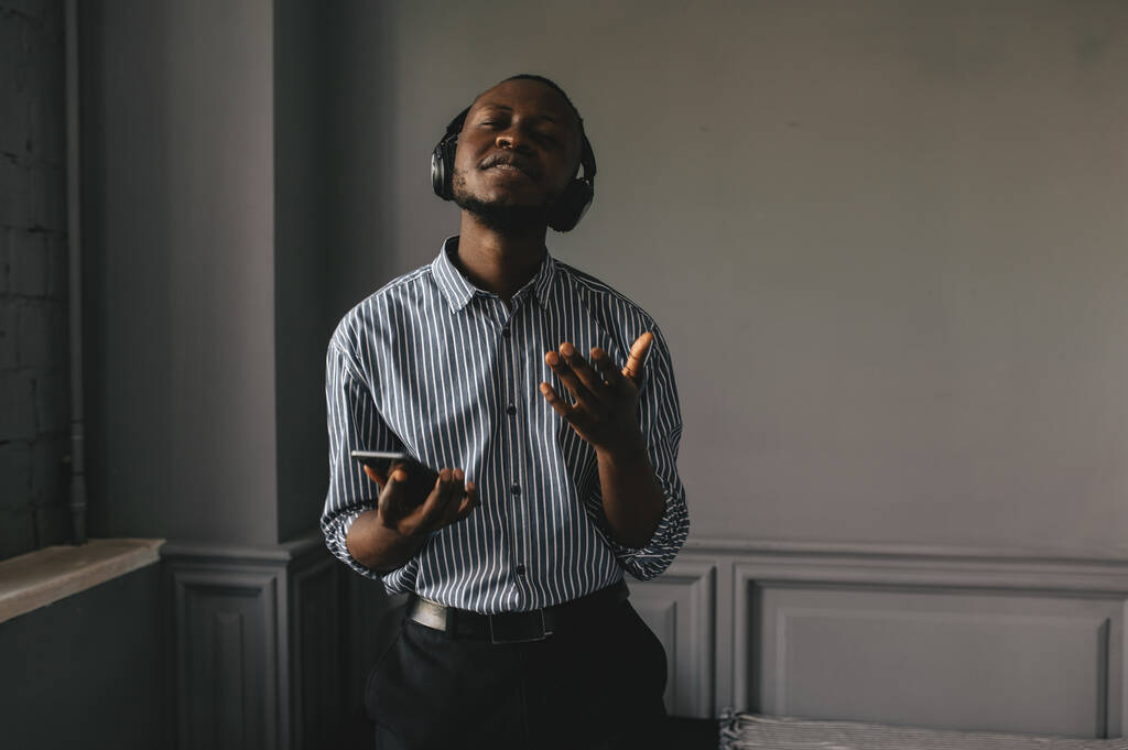 Joven africano escuchando música con auriculares inalámbricos y bailando en casa - Foto, Imagen