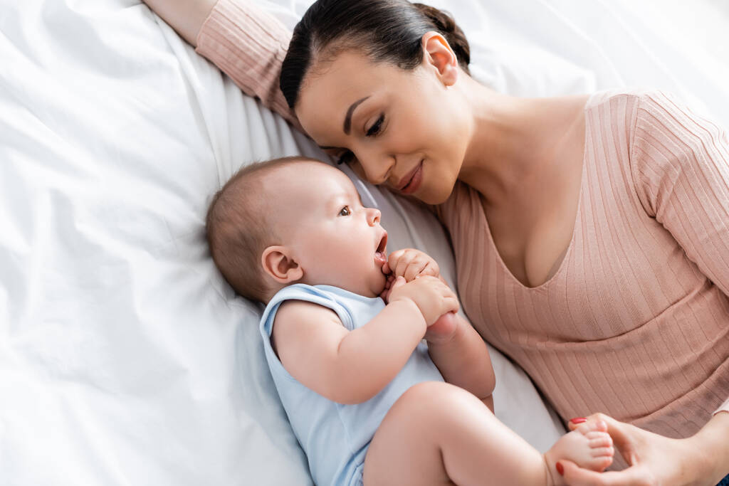 ベッドの上に寝そべっている赤ん坊を見ている母親の角度の高さ - 写真・画像