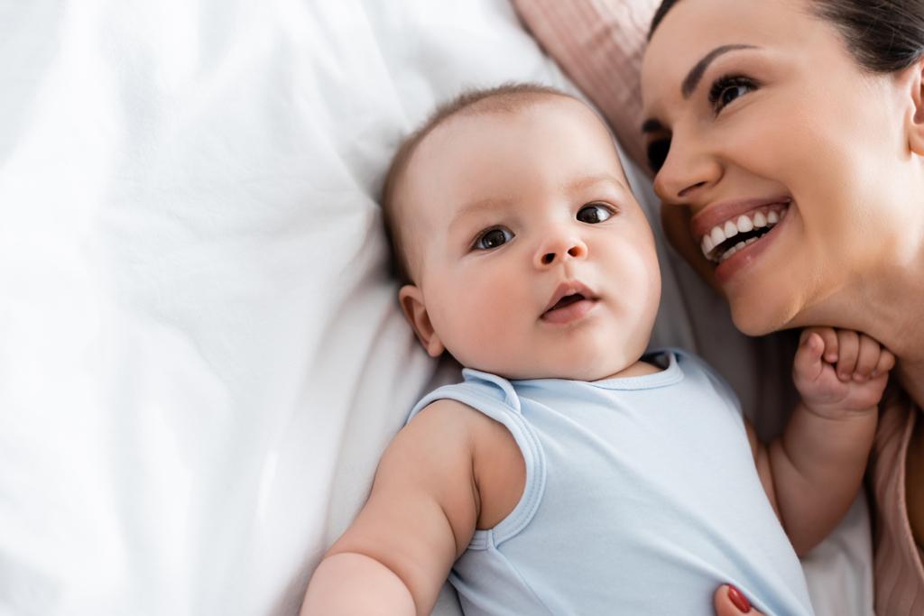 nad głową widok szczęśliwy matka uśmiecha się w pobliżu niemowlę dziecko leżąc na łóżku - Zdjęcie, obraz