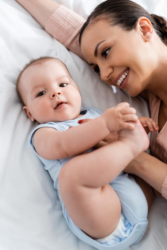 Blick von oben auf Mutter, die Säugling ansieht, während sie im Bett liegt - Foto, Bild