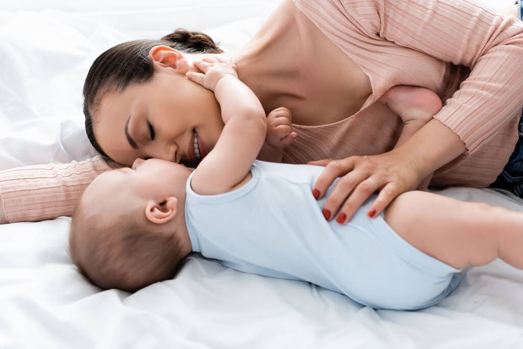 moeder met gesloten ogen liggend op bed met baby jongen  - Foto, afbeelding