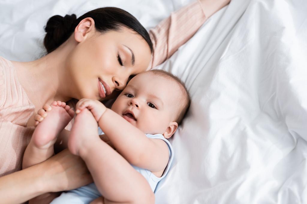 felső kilátás anya csukott szemmel feküdt az ágyon kisfiúval  - Fotó, kép