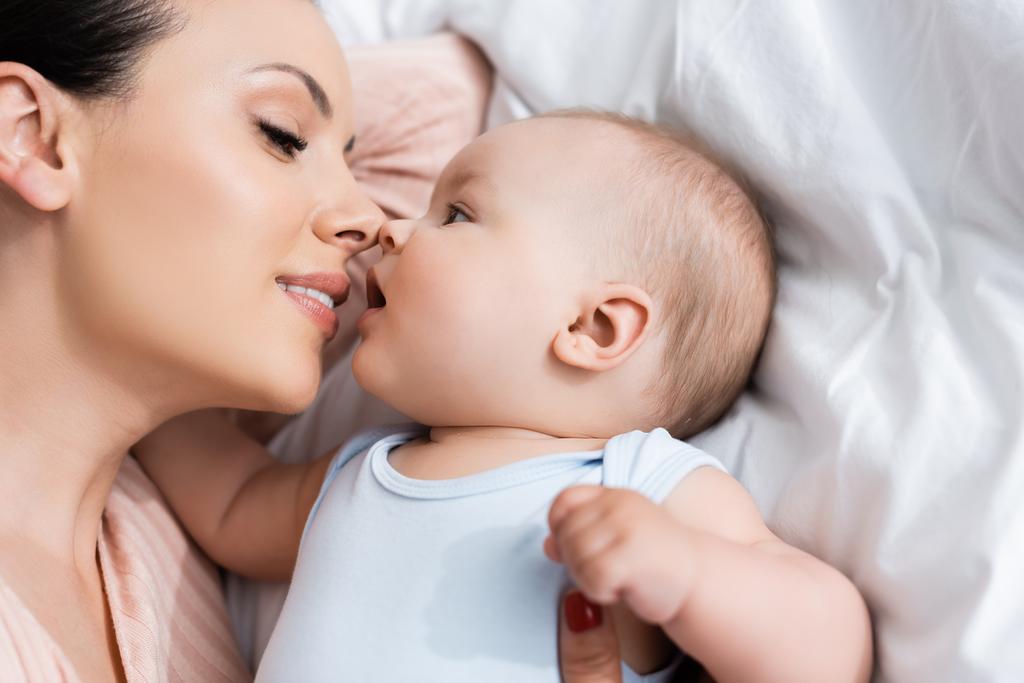 vista superior de la hermosa madre con los ojos cerrados acostado en la cama con el hijo bebé
  - Foto, Imagen