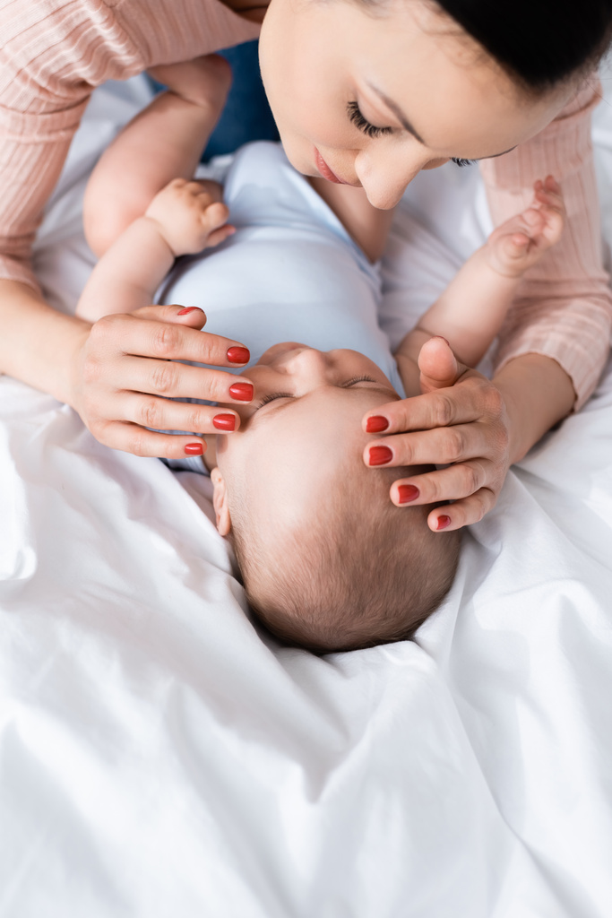 ベッドルームで可愛い赤ちゃんに触れる母親の角度の高い眺め - 写真・画像