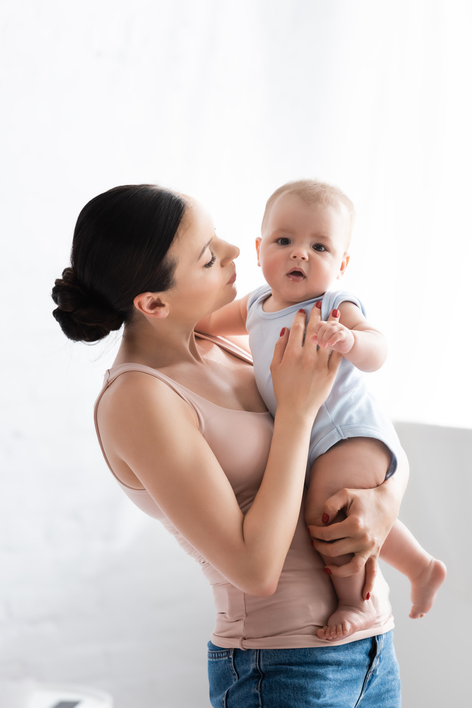 madre sosteniendo en brazos lindo bebé hijo con los pies desnudos
  - Foto, Imagen