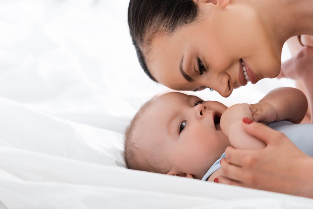 Lächelnde Mutter schaut Säugling im Schlafzimmer an  - Foto, Bild
