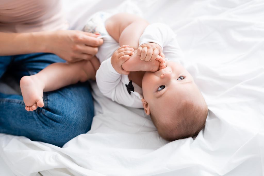selective focus of mother wearing baby romper on infant son sucking bare feet - Photo, Image