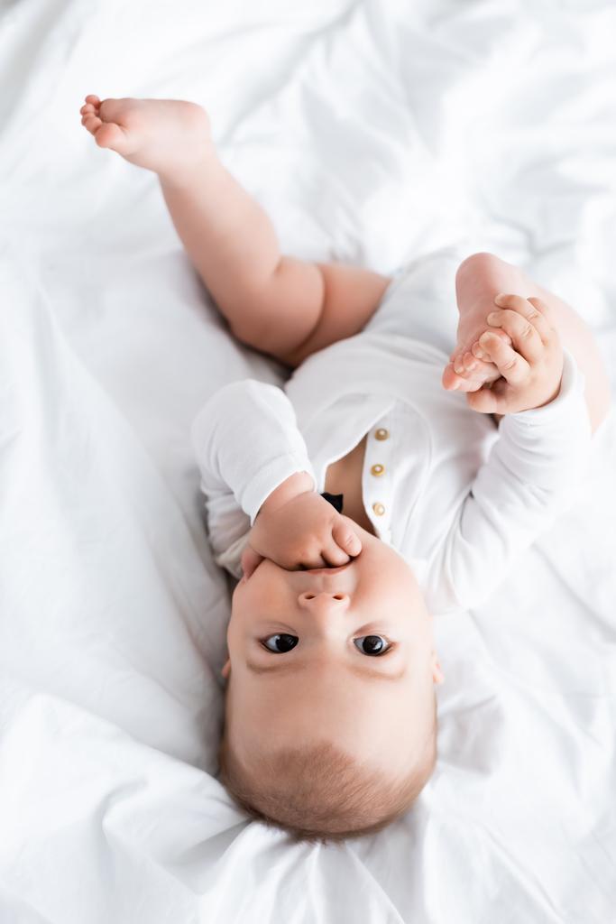 ベッドの上に横になりながら手を吸っている赤ん坊の姿 - 写真・画像