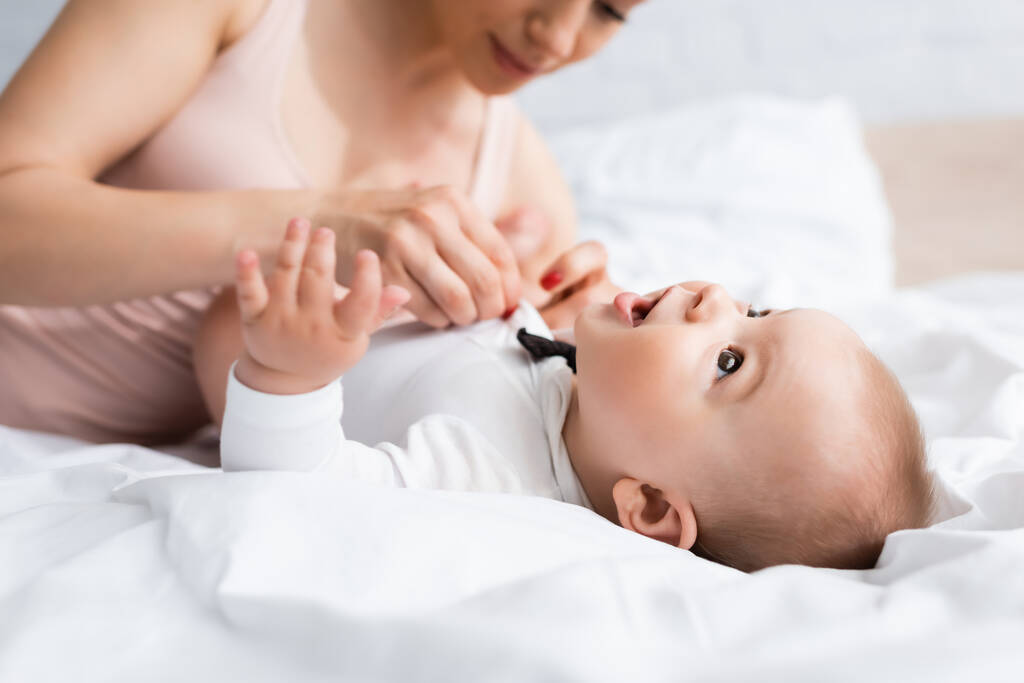 Mutter berührt Säugling im Babystrampler mit Fliege im Bett - Foto, Bild
