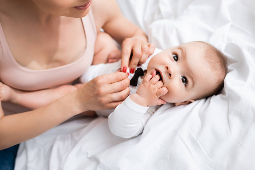 επιλεκτική εστίαση της μητέρας αγγίζοντας αξιολάτρευτο γιο στο μωρό romper με παπιγιόν στο κρεβάτι - Φωτογραφία, εικόνα