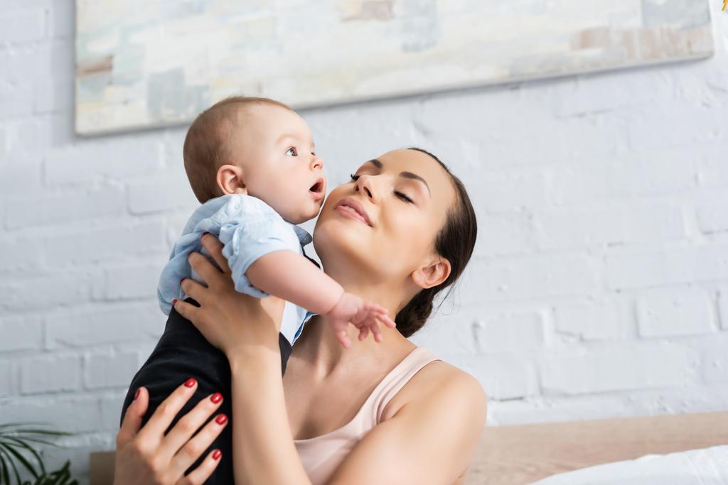 目を閉じて可愛い赤ちゃんの男の子を抱きしめる美しい母親 ロイヤリティフリー写真 画像素材