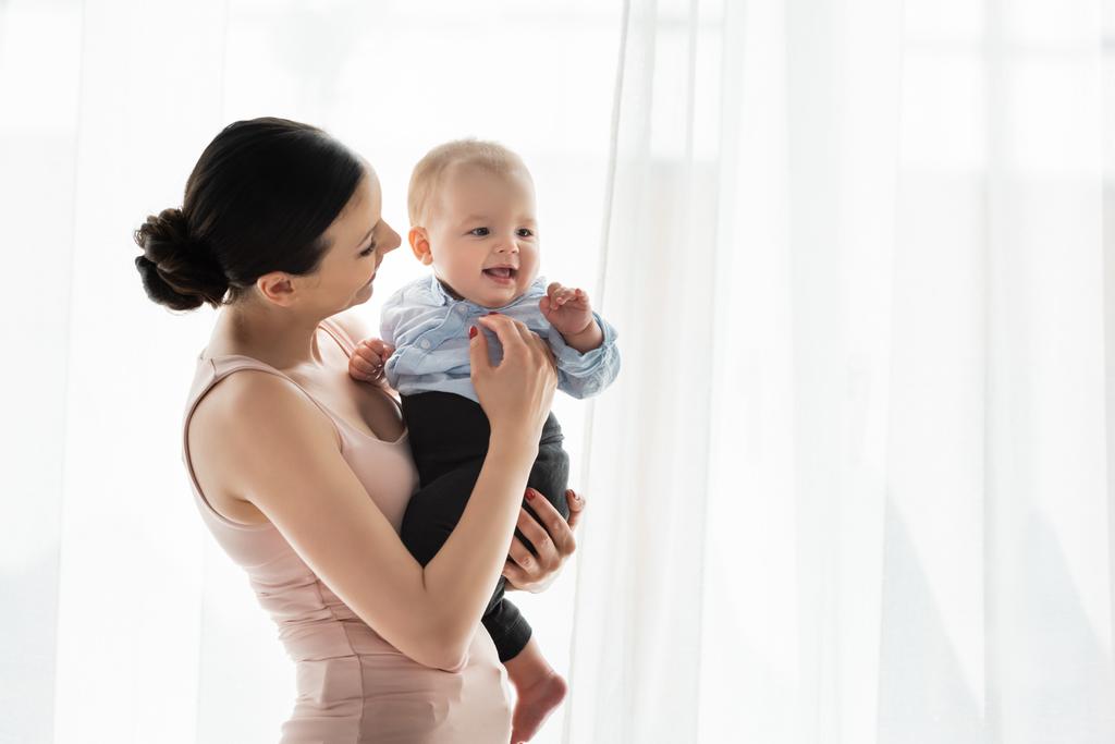 Lächelnde Mutter hält süßen Säugling in Babykleidung im Arm  - Foto, Bild