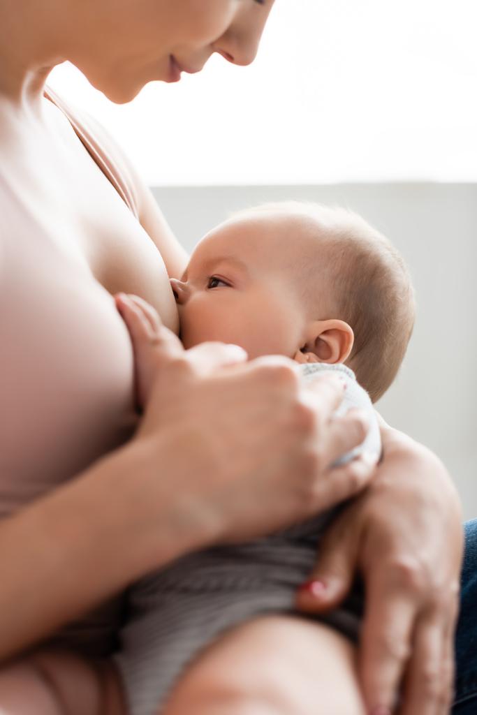 szelektív fókusz gondoskodó anya szoptatás baba fiú a hálószobában  - Fotó, kép