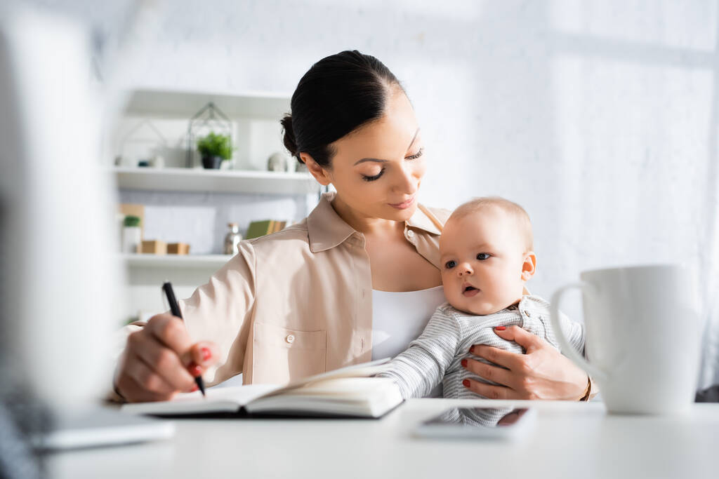 вибірковий фокус матері тримає ручку і дивиться на милого немовляти сина біля смартфона
 - Фото, зображення