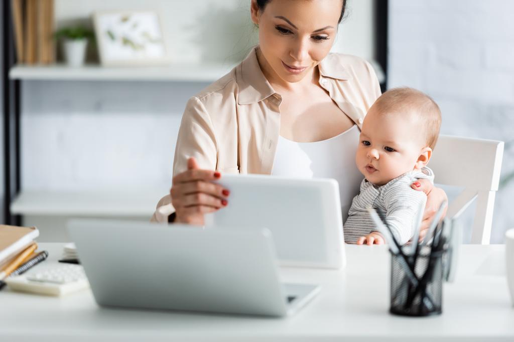 selektywne skupienie się matki trzymającej tablet cyfrowy w pobliżu niemowlęcia syna i laptopa  - Zdjęcie, obraz
