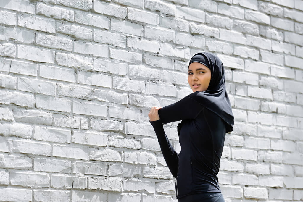 attractive muslim girl in hijab exercising near brick wall  - Photo, Image