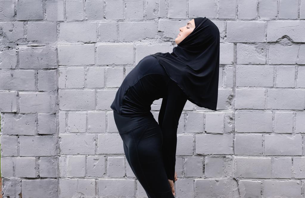 perfil de deportista musulmana estirándose cerca de muro de ladrillo
  - Foto, Imagen