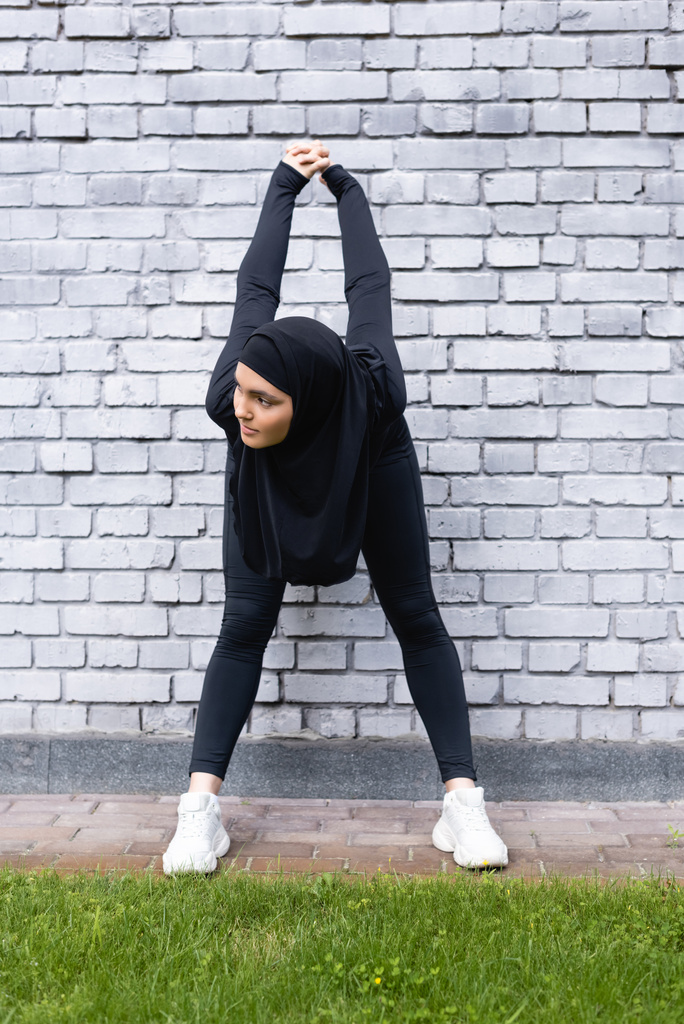 giovane sportiva musulmana che esercita vicino al muro di mattoni e erba verde - Foto, immagini