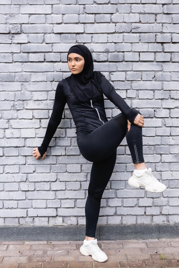 giovane sportiva musulmana in hijab che lavora vicino al muro di mattoni  - Foto, immagini