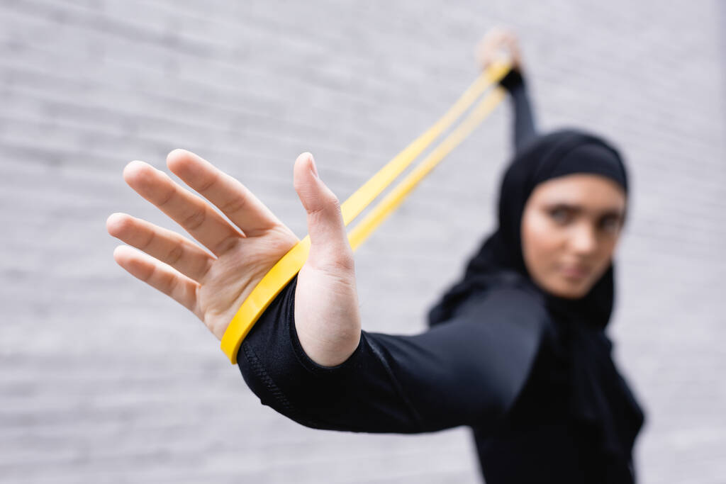 selektivní zaměření arabské sportovkyně v hidžábu cvičení s pásmem odporu u cihlové zdi - Fotografie, Obrázek