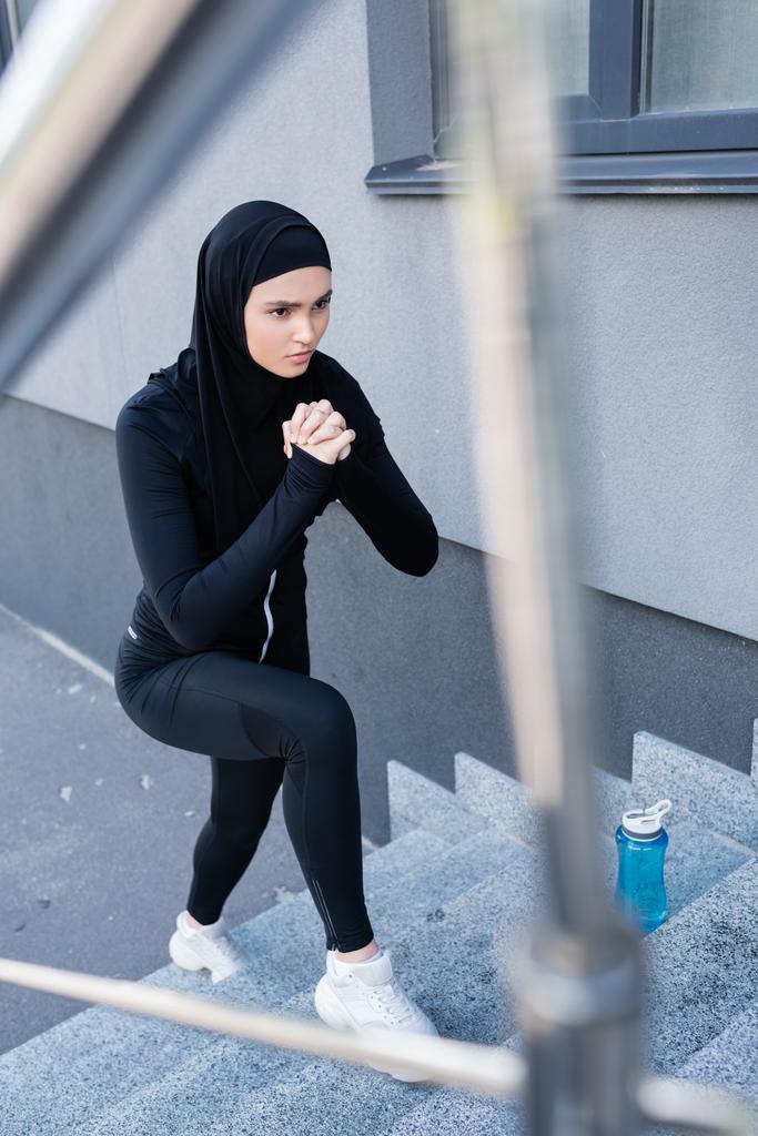 スポーツボトルの近くの階段で運動するヒジャーブのイスラム教徒女性の選択的焦点  - 写真・画像