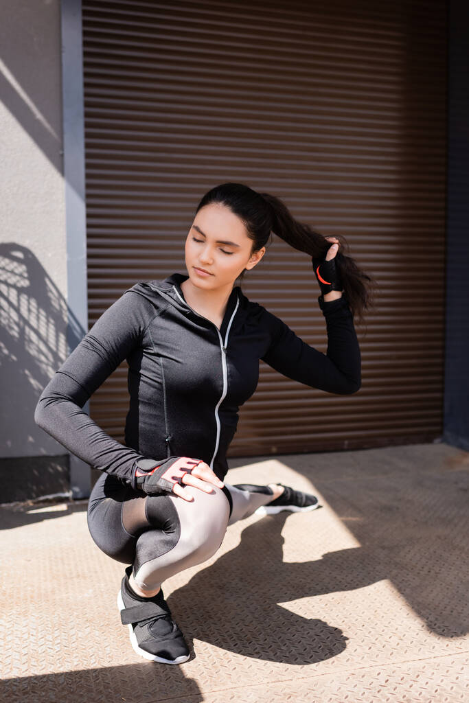 selective focus of beautiful young sportswoman stretching outside while touching hair - Photo, Image