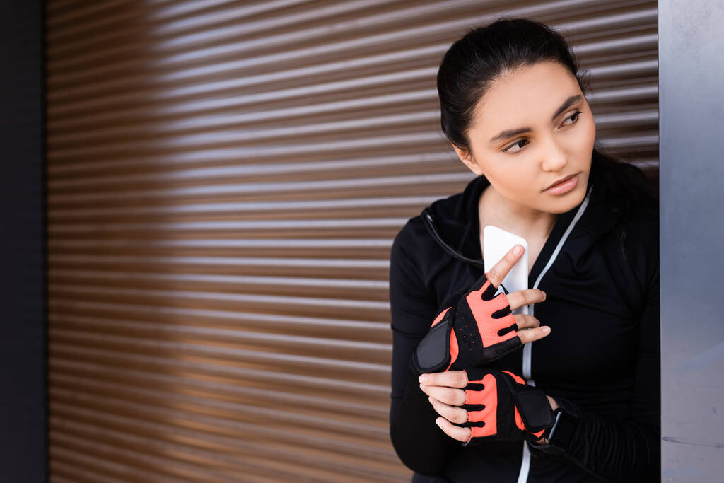 junge Sportlerin hält Smartphone in der Hand und schaut weg - Foto, Bild