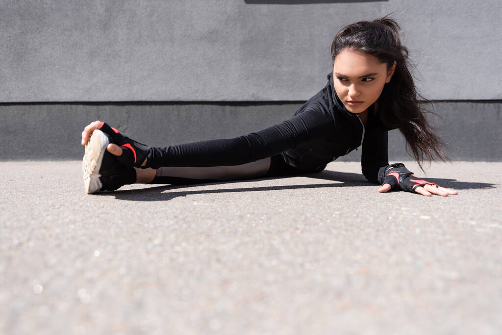 selectieve focus van mooie jonge sportvrouw stretching op asfalt - Foto, afbeelding
