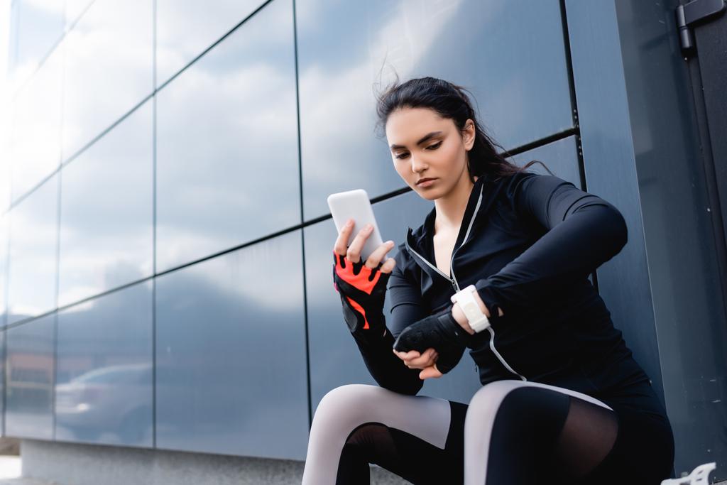 jonge sportvrouw met smartphone en op zoek naar fitness tracker - Foto, afbeelding